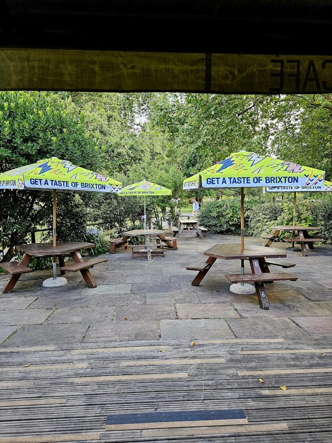 Empty picnic benches under green parasols on the paved terrace